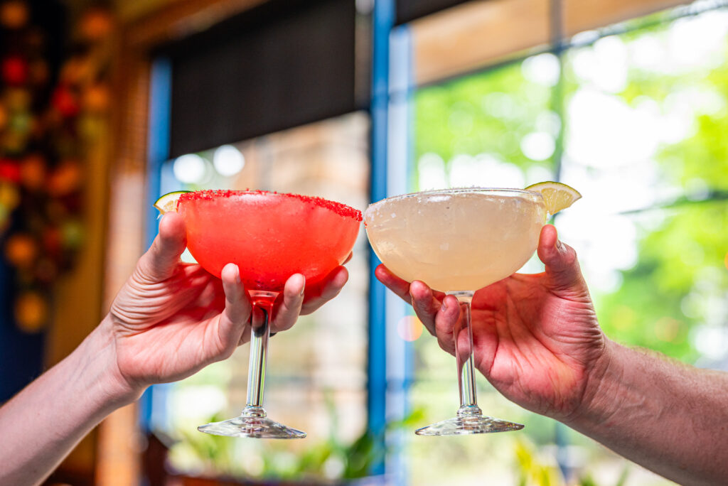 2 friends clinking a Strawberry and Original flavored margarita