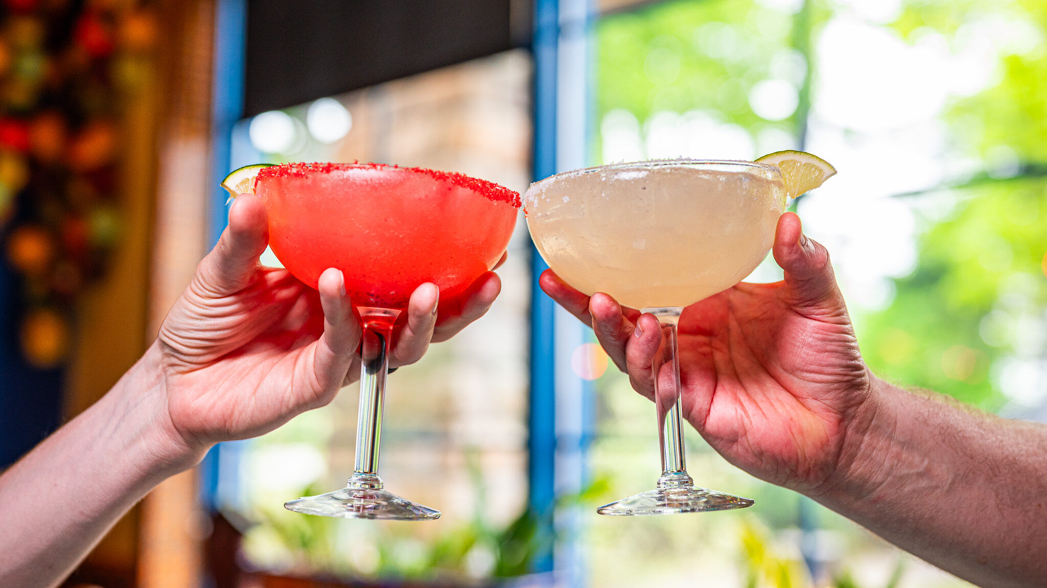2 friends clinking a Strawberry and Original flavored margarita