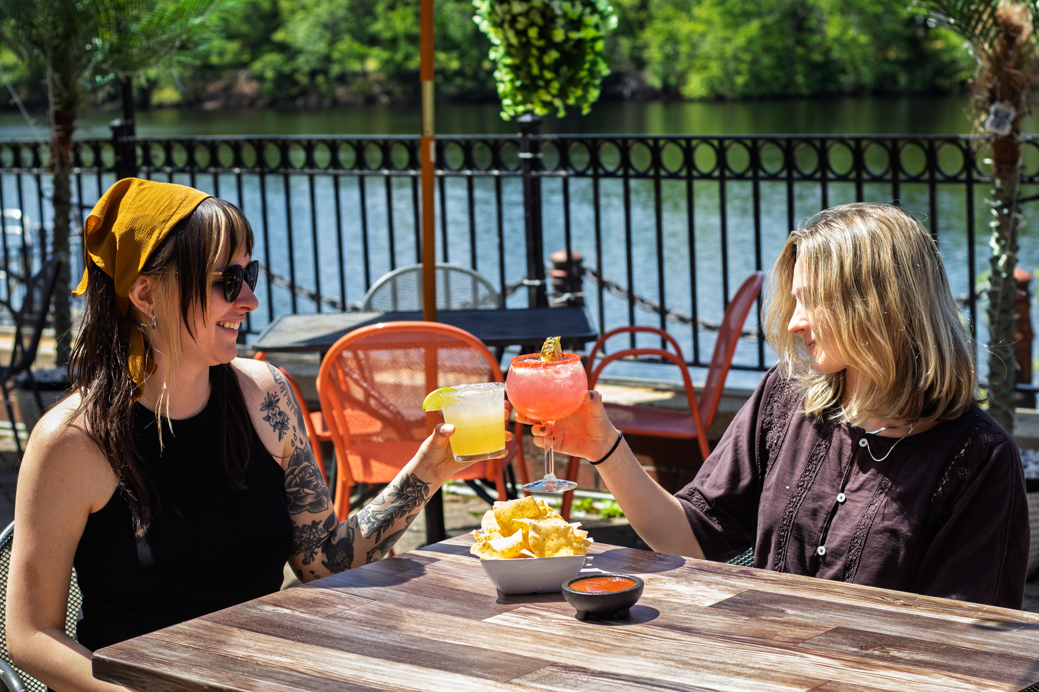 Two people drinking margaritas on a patio by the river.